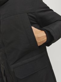 Juodas paminkštintas paltas su užtrauktuku, šoniniais kišenėmis ir tekstūruota medžiaga. Dizainas apima aukštą apykaklę ir raštuotas rankoves.