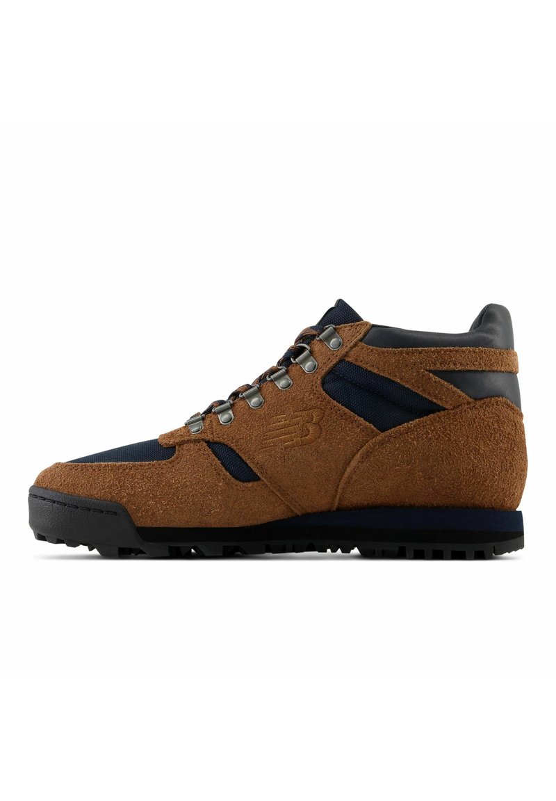 Chaussure de randonnée en daim marron et noir avec œillets en métal, semelle robuste, et logo New Balance sur le côté, montrée en profil latéral.