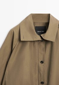 Beiger Mantel zum Knöpfen mit weitem Kragen, sichtbaren Nahtdetails und schwarzem Etikett mit der Aufschrift "Massimo Dutti" im Nackenbereich.