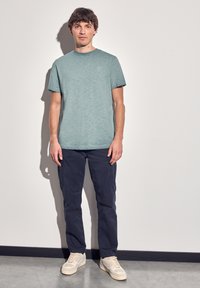 Camiseta de manga corta azul claro combinada con pantalones azul oscuro y zapatillas de color claro. La tela tiene una sutil textura y un corte relajado.