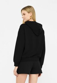 Must be a black hoodie, mille kõrge krae ja pikad varrukad, lõdva istuvusega ja sooniku äärisega. Sile tekstuur, minimalistlik disain, kombineeritud mustade lühikeste pükstega.
