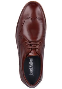 Chaussure habillée en cuir marron avec des détails perforés, bout rond, lacets et semelle de couleur claire contrastante. Marque visible à l'intérieur.