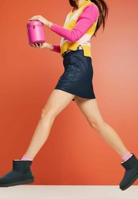 Obuwie: czarne botki za kostkę o fakturowanym wykończeniu. Strój zawiera różowo-żółtą kamizelkę w paski na długim różowym rękawie, w połączeniu z granatową spódnicą.