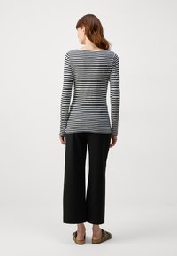Langermet topp i svart og hvitt striper, tettsittende i midjen, kombinert med vidde svarte bukser og grønne slip-on sko. Glatt tekstur.