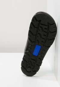 Black shoe sole with textured tread pattern and a blue accent element. Material appears rubberized with a smooth finish.