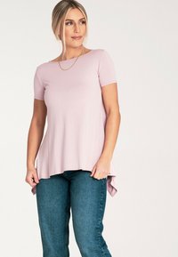 Jasnoróżowa bluzka z krótkim rękawem, okrągłym dekoltem i asymetrycznym dołem, w zestawie z ciemnoniebieskimi dżinsami. Gładka tekstura, luźny krój.