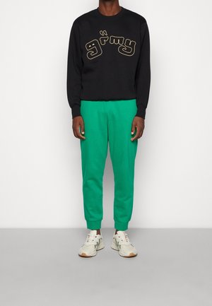 Svart sweatshirt med "grimy" guldtext, kombinerad med gröna smala sweatpants och ljusa sneakers.