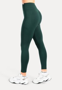 Groene leggings met hoge taille, gemaakt van rekbare stof, met een gladde textuur en een aansluitend ontwerp, gecombineerd met witte sportschoenen.