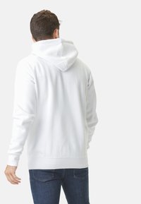 Sweatshirt à capuche blanche avec une texture douce, des manches longues et une taille côtelée. Il dispose d'une poche kangourou et d'une capuche avec cordon de serrage.