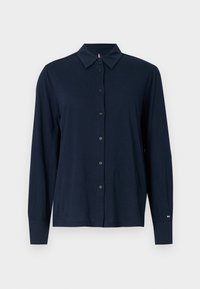 Navy niebieska koszula z długim rękawem na guziki z kołnierzykiem w kształcie szpica, wykonana z miękkiego materiału, z czarnymi guzikami i małym logo na rękawie.