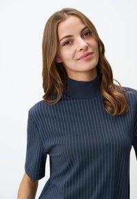Granatowa bluzka z krótkimi rękawami, wysokim prążkowanym kołnierzem i cienkimi pionowymi paskami. Miękka tekstura z dopasowanym krojem. Znaczący kontrast kolorów w paskach.