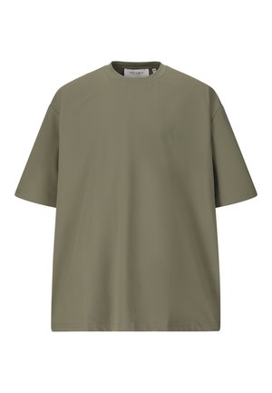 Ung mand går, iført en olivengrøn T-shirt, sorte bukser og hvide sneakers mod en ensfarvet hvid baggrund.