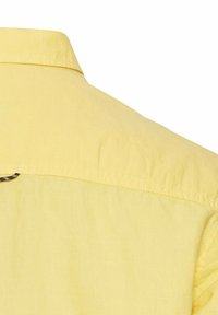 Geel shirt met korte mouwen, gemaakt van een zachte stof en met een kraag aan de achterkant. Het heeft een eenvoudig ontwerp en subtiele stiksels langs de naden.