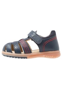 Sandalia de cuero azul marino con recortes, acentos de costura roja, tira de velcro ajustable y suela de goma flexible con agarre texturizado.