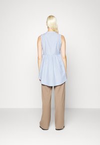 Haut sans manches rayé bleu et blanc avec une taille froncée, ourlet arrière long, associé à un pantalon large beige clair. Texture de tissu lisse.