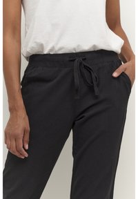 Czarne spodnie z teksturowanej tkaniny z elastycznym pasem, sznurkiem do regulacji i bocznymi kieszeniami; w połączeniu z prostą białą bluzką.