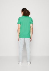 Polo shirt verde a maniche corte in cotone, abbinato a jeans azzurri e sneakers bianche. Design semplice, forma aderente, senza fantasie.