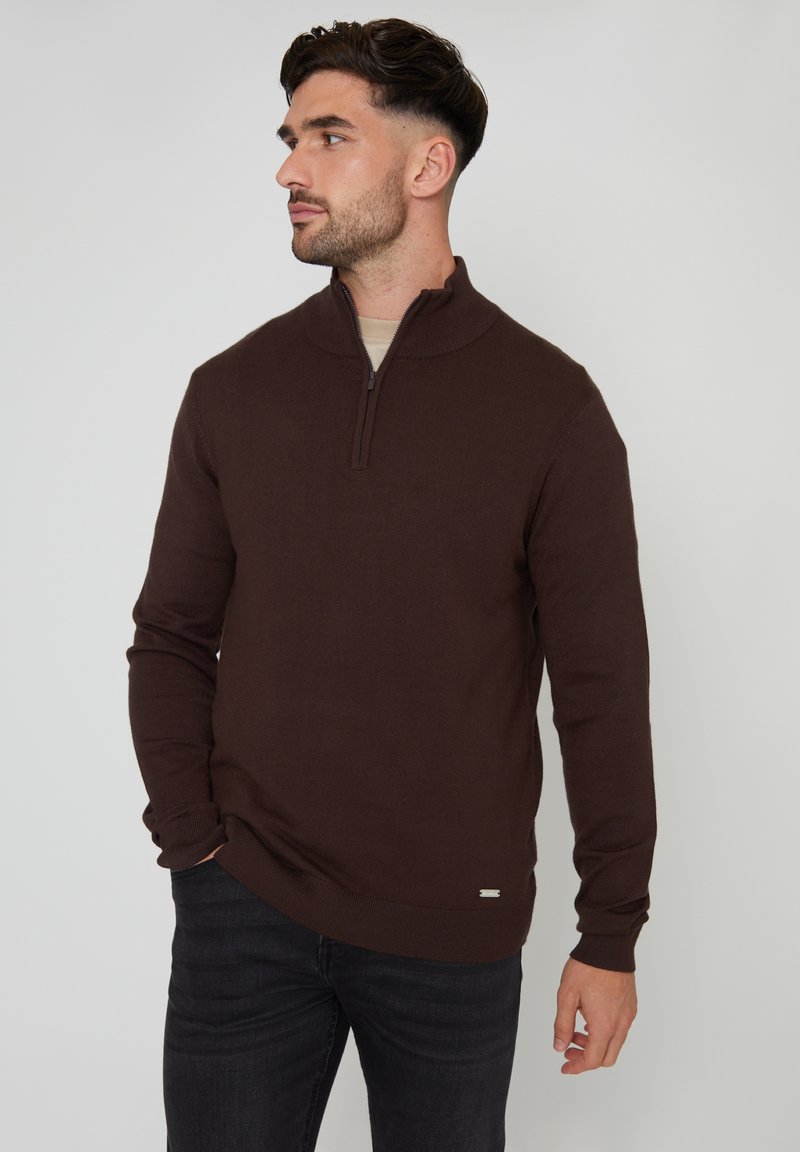 Maglione marrone a maglia con un colletto a mezza zip, polsini e orlo a coste. Abbinato a jeans di denim scuro. Tessuto testurizzato con una finitura liscia.