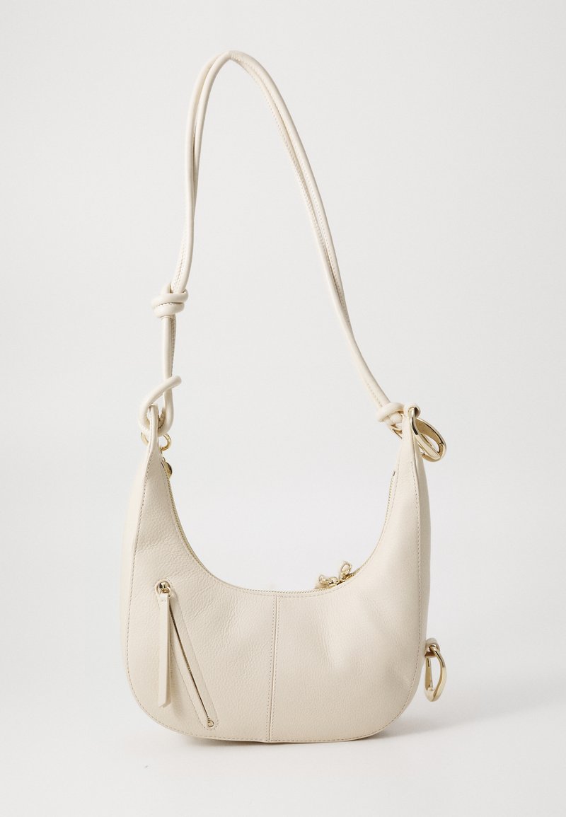 Cream leather shoulder bag with a curved shape, featuring a zippered front pocket, gold accents, and a knotted shoulder strap.