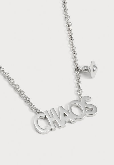 Collier chaîne en argent avec un grand pendentif portant les lettres CHAO5 et un petit charm en forme de cœur sur un fond clair.