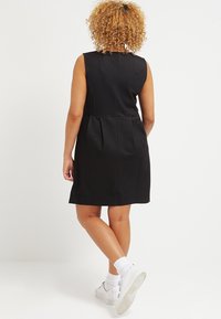 Abito nero senza maniche con una forma leggermente svasata, tessuto testurizzato, pieghe in vita, abbinato a sneaker bianche e calze alla caviglia.