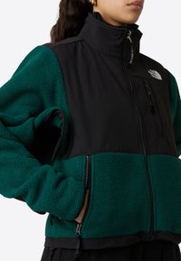 Giacca in fleece nera e verde con colletto alto, tasche con zip, tessuto testurizzato e design a pannelli a contrasto.