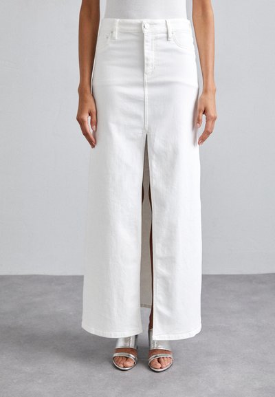 Jupe maxi en denim blanc avec une fente frontale, taille haute et texture subtile. Assortie à des sandales à bride métalliques.