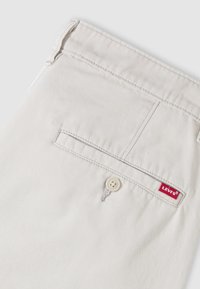 Poche arrière d'un pantalon Levi's beige clair avec fermeture à bouton et petite étiquette rouge du logo Levi's sur le bord de la poche.