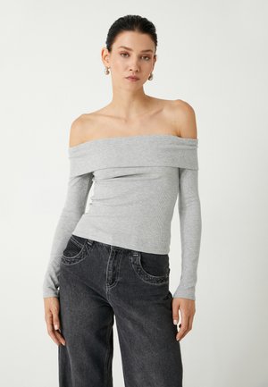 Graues, schulterfreies, geripptes Oberteil mit langen Ärmeln, taillierter Passform, kombiniert mit dunklen, weit geschnittenen Jeans mit Fronttaschen und Stichdetails.