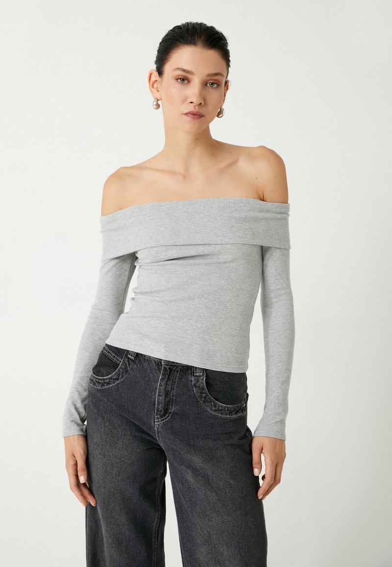 Top grigio a coste off-the-shoulder con maniche lunghe, design attillato, abbinato a jeans a gamba larga scuri con tasche frontali e dettagli di cucitura.