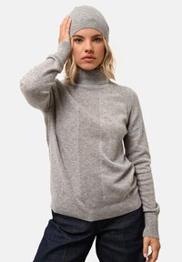 Szary sweter z dzianiny z wysokim kołnierzem i prążkowanymi akcentami, o wyraźnej strukturze. Nosi się z pasującą szarym czapką. Casualowy strój.