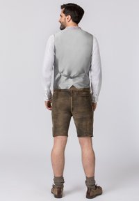 Graue Satinweste mit einer Rückenschnalle, kombiniert mit braunen Ledershorts und knielangen grauen Socken, getragen mit braunen Schuhen.