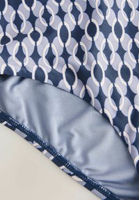 Gros plan sur un tissu avec un motif d'ovales entrelacés bleu marine et gris clair, montrant des coutures détaillées et une texture lisse.