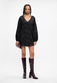 Melna kleita ar ziedu rakstu, ar V veida kakla izgriezumu, garām bumbierveida piedurknēm un brīvu piegriezumu. Kombinēta ar potīšu augstuma bordo lakota ādas zābakiem.