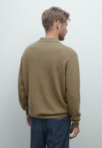Brauner, weicher Pullover mit Kragen und langen Ärmeln, der eine lockere Passform hat, kombiniert mit blauen Jeans.