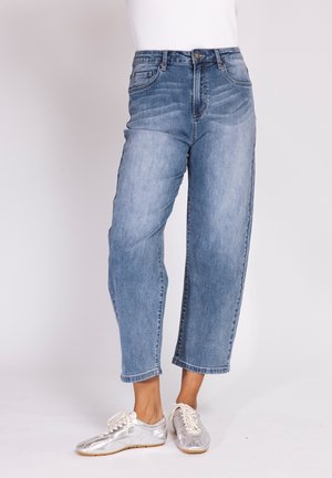 Woman wearing light blue cropped jeans and silver sneakers, standing against a plain light background.