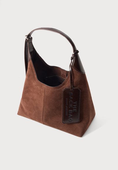 Кафява велурена чанта с тъмна кожена дръжка и етикет с надпис "THE SACK BAG MARC JACOBS,", отворен връх, показващ вътрешен цип джоб.