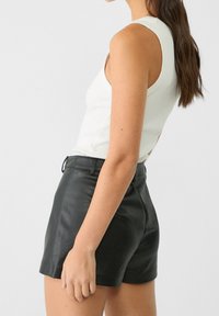 Zwarte leren shorts met een getailleerd ontwerp, voorzien van een mid-rise taille en een gladde textuur. Gecombineerd met een witte geribbelde tanktop.
