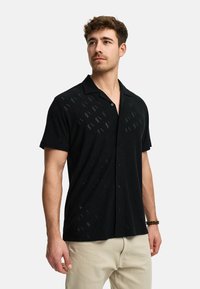 Black short-sleeve shirt made from textured fabric featuring patterned cutouts and front buttons, with a classic collar and relaxed fit.