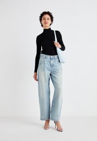 Juoda raukšlėta turtleneck palaidinė, šviesiai mėlyni platūs džinsai su išblukimu ir skaidrūs kulniukai. Laiko šviesiai mėlyną petinę rankinę.