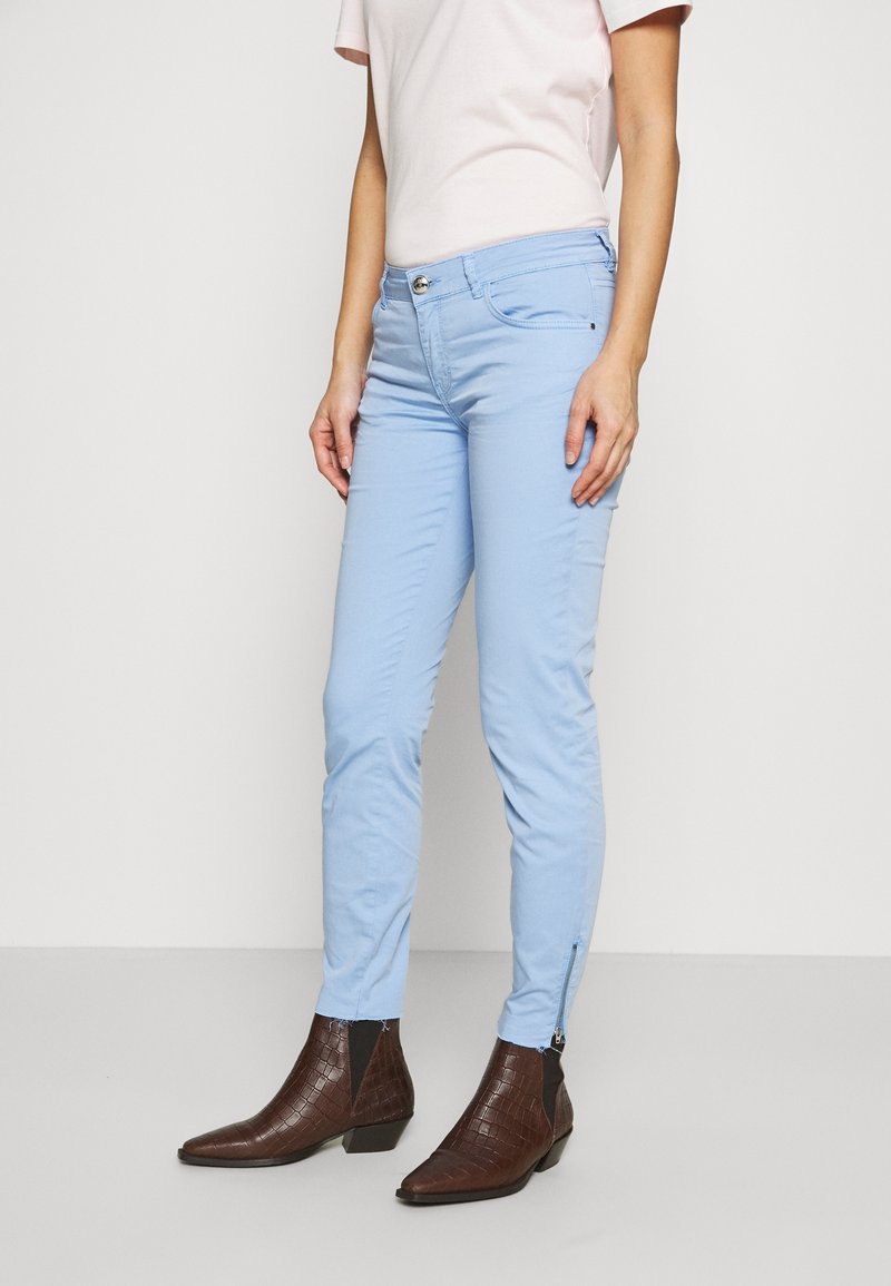 Pantalons ajustés bleu clair avec une fermeture éclair à la cheville, associés à un haut rose pâle et des bottines marron foncé à la finition texturée.