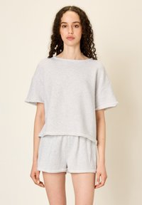 Šviesiai pilkas medvilnės dviejų dalių komplektas, kuriame yra trumpomis rankovėmis marškiniai su plačiu siluetu ir laisvi šortai su elastinga juosmens juosta ir sukneigtomis kraštinėmis.