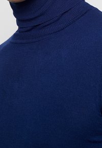 Närbild på en person som bär en marinblå ribbad polotröja, som visar detaljerad tygtextur och halsområde.