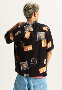 Short-sleeve black shirt with a unique pattern of orange and white graphic squares. Made from lightweight fabric with a relaxed fit.