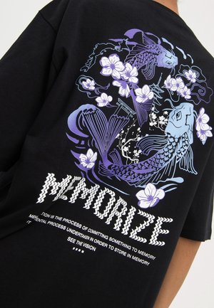 Sort t-shirt i sort bomuld med et grafisk print i lilla og hvid af koi-fisk, blomster og japanske elementer; teksten lyder "MEMORIZE" med fed skrift.