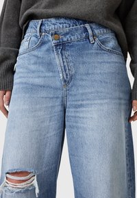 Ljusbl å denim jeans med hög midja och avslappnad passform, med knäppning framtill, två fickor och slitna detaljer vid knäna.