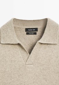 Beige kasjmier trui met een geribde kraag, V-hals ontwerp en een zachte textuur. Labels geven het merk en de materiaalsamenstelling aan.