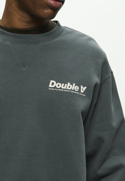Sweatshirt vert foncé avec une finition texturée, présentant un col rond côtelé et un logo blanc sur la poitrine gauche.