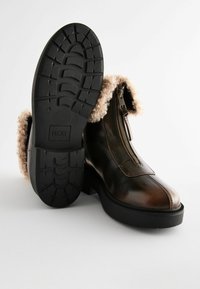 Brown leather ankle boots with faux fur lining, side zipper, and textured black rubber sole. Smooth finish with contrasting stitching details.