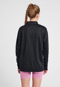 Zwart sportshirt met lange mouwen van een textuurstof, met een opstaande kraag en een ontspannen pasvorm, gecombineerd met roze compressieshorts.